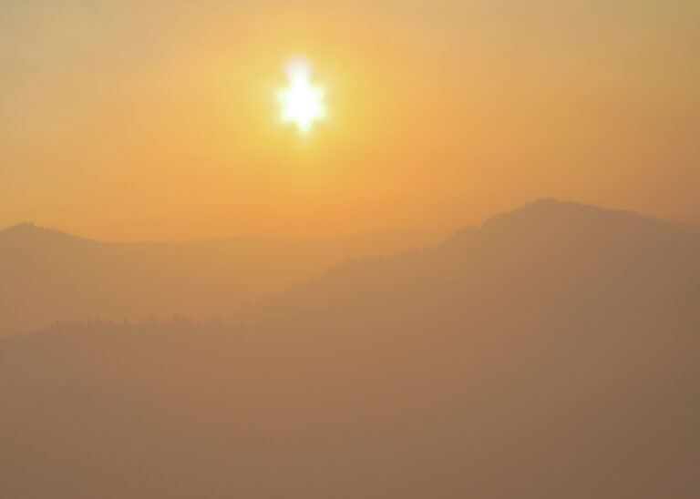 Bright sun covered in orange smoke haze, above mountain horizon.